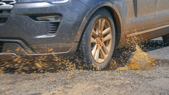 CLOSE UP Driving car hits a pothole in asphalt road and splashes muddy rainwater