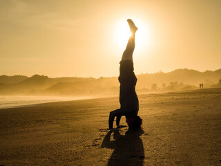 SILHOUETTE, LENS FLARE: Sunbeam shines from behind a man doing yoga headstand