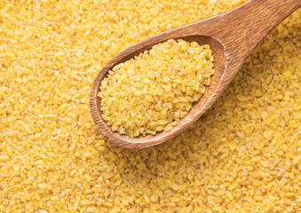 Raw organic healthy yellow bulgur seeds on wooden spoon in kitchen.Macro.