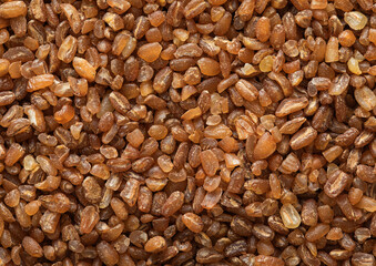 Brown raw healthy bulgur grain seeds textured background.Macro.