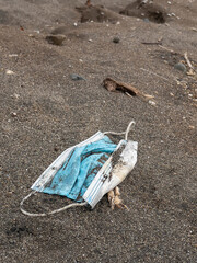 CLOSE UP, DOF: Used medical mask lying on a sandy beach after being washed up