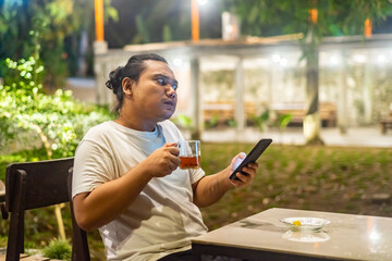 Young Asian man, digital nomad working remotely from cafe, using laptop and smartphone. young Asian men are hanging out in a cafe with a nature theme at night