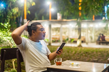 Young Asian man, digital nomad working remotely from cafe, using laptop and smartphone. young Asian men are hanging out in a cafe with a nature theme at night