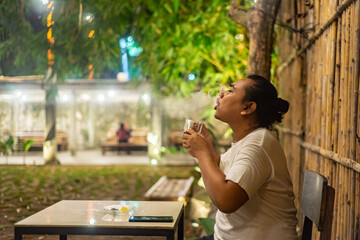 Young Asian man, digital nomad working remotely from cafe, using laptop and smartphone. young Asian men are hanging out in a cafe with a nature theme at night