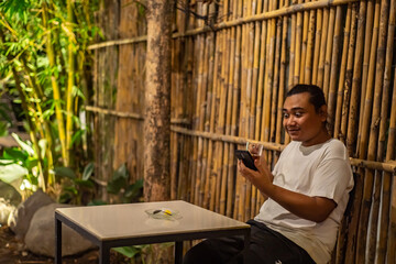 Young Asian man, digital nomad working remotely from cafe, using laptop and smartphone. young Asian men are hanging out in a cafe with a nature theme at night