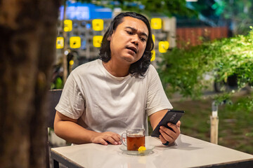 Young Asian man, digital nomad working remotely from cafe, using laptop and smartphone. young Asian men are hanging out in a cafe with a nature theme at night