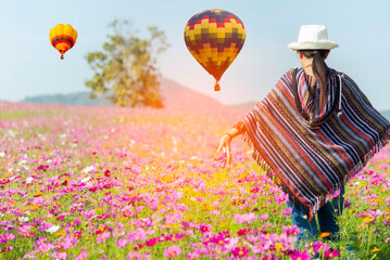 Lifestyle traveler women raise hand feeling good relax and happy freedom and see the fire balloon outdoors the nature tea and cosmos farm in the sunrise morning. Travel and summer Concept