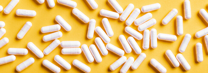 White medical capsules on yellow background.