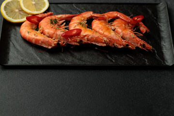 Large cooked king prawns on a black background. Lemon slices