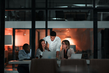 Teamwork, laptop and business people in office at night with stock market charts for corporate...