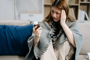 Young Asian woman suffering from flu symptoms, covered with a blanket on a sofa. Concept of...
