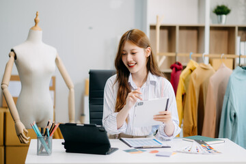 Fashion designer woman talking smart phone and using laptop with digital tablet computer in modern studio