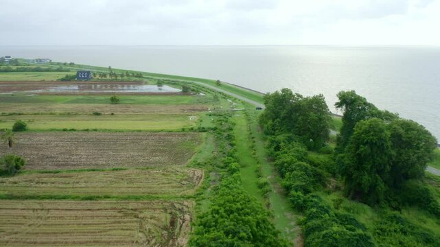 Aerial: Sea dyke view along the road, camera tilt ocean reveal, North Atlantic Ocean and Nickerie Suriname