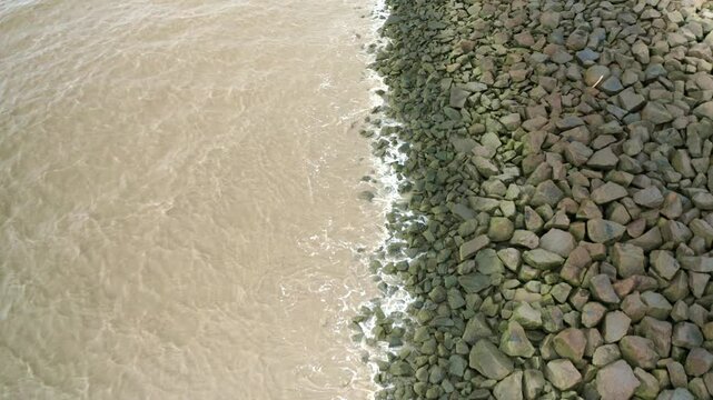 Sea waves hitting rocks on a sea dyke, drone flying backwards
