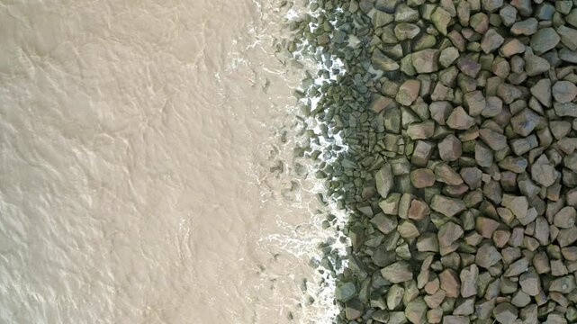 Sea waves hitting rocks on a sea dyke, drone ascending overhead shot