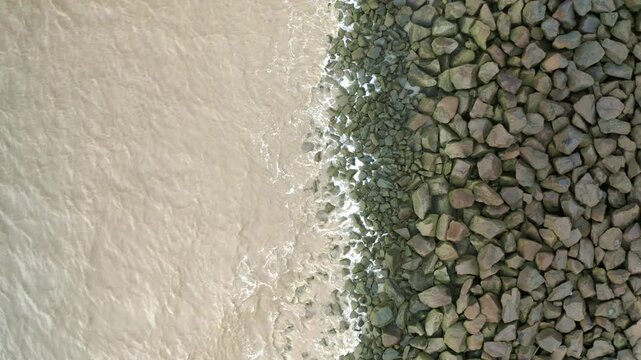 Sea waves hitting rocks on a sea dyke, drone descending overhead shot