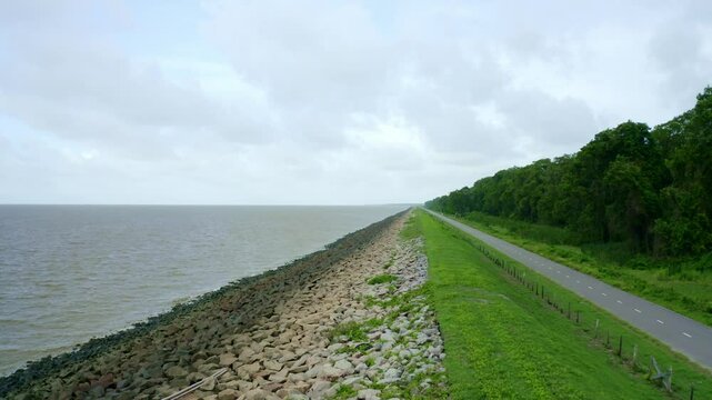 Aerial: Sea dyke view along the asphalt road, drone flying backwards, North Atlantic Ocean and Nickerie Suriname