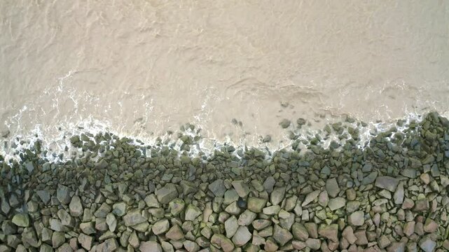 Sea waves hitting rocks on a sea dyke, overhead drone shot descending