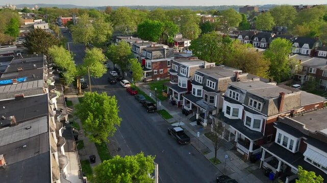 Aerial footage of a quiet residential neighborhood with tree-lined streets, charming row houses, and parked cars. American city suburb row houses.