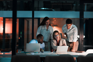 Conversation, laptop and business people in office at night with stock market charts for corporate investment. Discussion, computer and financial advisors work on company profit report with deadline.