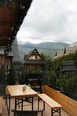 A charming view of a wooden terrace with a table and benches, overlooking traditional wooden houses with the Tatra Mountains in the background. The scene captures the peaceful ambiance of Zakopane