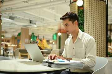 Handsome businessman chatting with partners or clients on his laptop in cafeteria