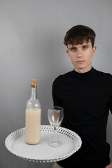 A young waiter in studio holding a bottle and glass on a tray