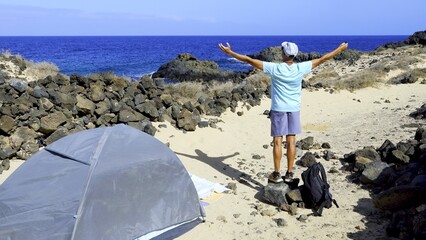 Backpacker tourist looks at the ocean and enjoys the landscape with open arms. Summer and feeling...