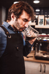 A man professionally brews coffee in a glass teapot using a filter using the drip method under a press
