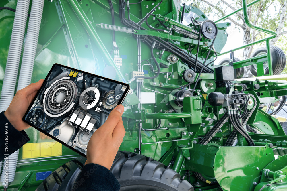 Poster serviceman with digital tablet next to combine harvester with open hood.
