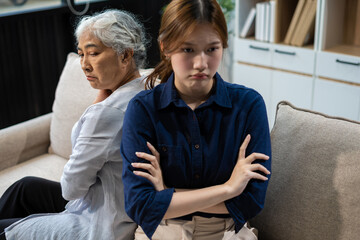 Granddaughter and her grandmother sitting on the sofa, angry at each other, their backs to each other.