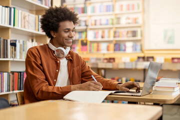 Happy Black student guy prepare assignment, learning theory, using laptop while studying in college...