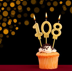 Number 108 birthday candle - Cupcake on black background with out of focus lights