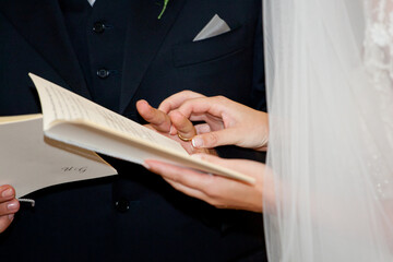 Newlywed couple holding hands and reciting their vows from a book during a religious wedding ceremony