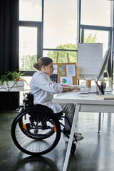 A young businesswoman in a wheelchair is working on her computer in a modern office space.