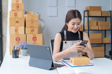 Delivery business. happy modern female in White Shirt checking order with laptop and holding a cup of coffee parcels using smartphone applications in the warehouse