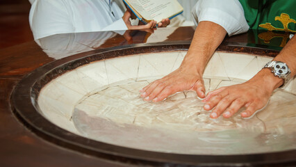 Priest blessing water inside a baptismal font during a religious ceremony in a church