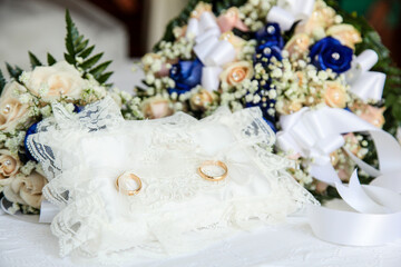 Two gold wedding rings are resting on a white lace pillow, symbolizing the union of two people in...