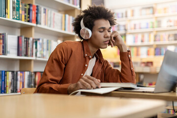 College burnout. Tired African American guy sitting at laptop, learning in university library indoors. Higher education problems