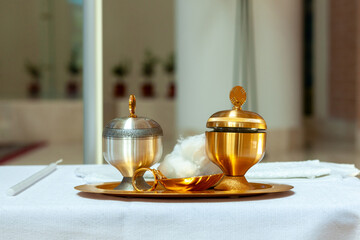 Golden and silver chalice with holy water and chrism oil for baptism on the altar