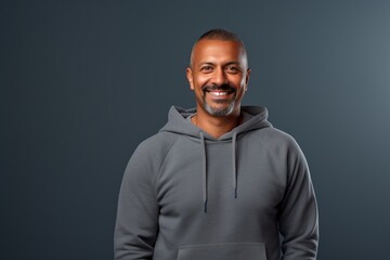 Fototapeta premium Portrait of a smiling indian man in his 40s sporting a comfortable hoodie over minimalist or empty room background