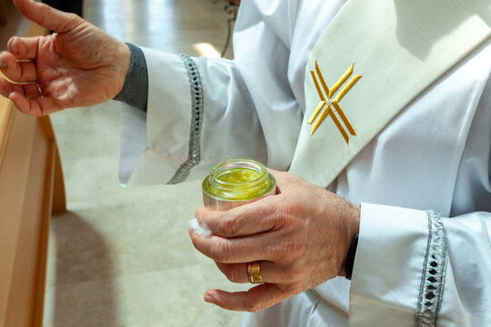 Religious ceremony, priest in white robe holding jar of chrism oil