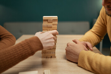 Friends build a tower from wooden blocks on the table sitting in living room, close-up. Board game