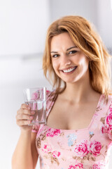 Young cute woman drinking pure water from glass in her kitchen. 