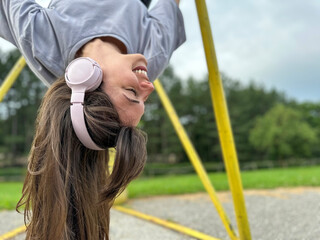Obraz premium Pretty young woman hanging upside down with her headphones on, celebrating love and life, enjoying summer and autumn, healthy lifestyle concept 