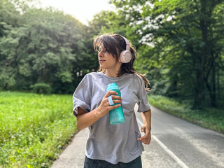 Naklejka premium Young women jogger with water bottle in early morning spring sunshine running in forest road with headphones. Concept healthy living.