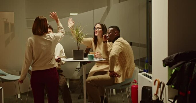 A delightful female employee saying buy to her colleagues, exchanging high fives and warm greetings before leaving work, fostering a positive and supportive work environment.