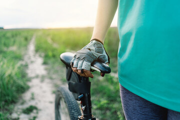 The person is the middle of an outdoor bike ride. The image focuses on the detail of the glove and the seat and adventure experienced while riding a bike through