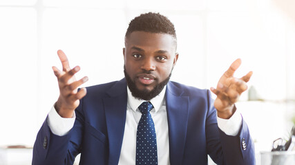 Portrait of angry african businessman looking at camera, gesturing and talking, scolding employees at office