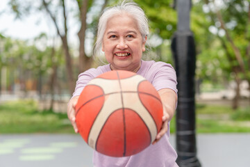 Naklejka premium Cheerful active senior woman playing basketball in the urban outdoor basketball court, healthy life concepts